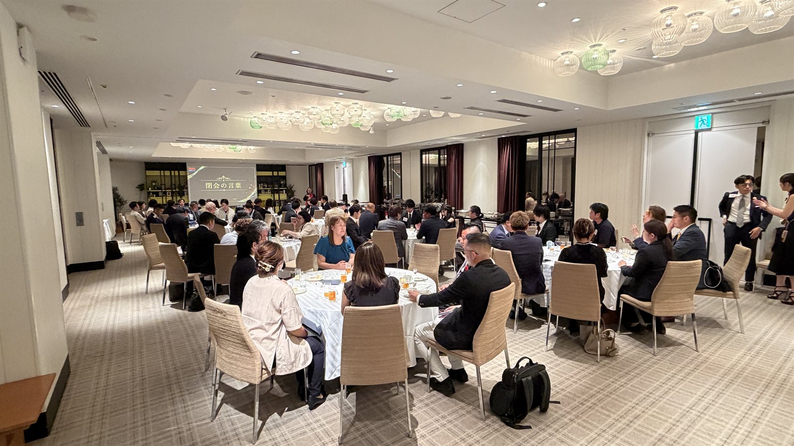 Full view of the NEXIA founding celebration venue, with guests seated at round tables listening to the opening remarks